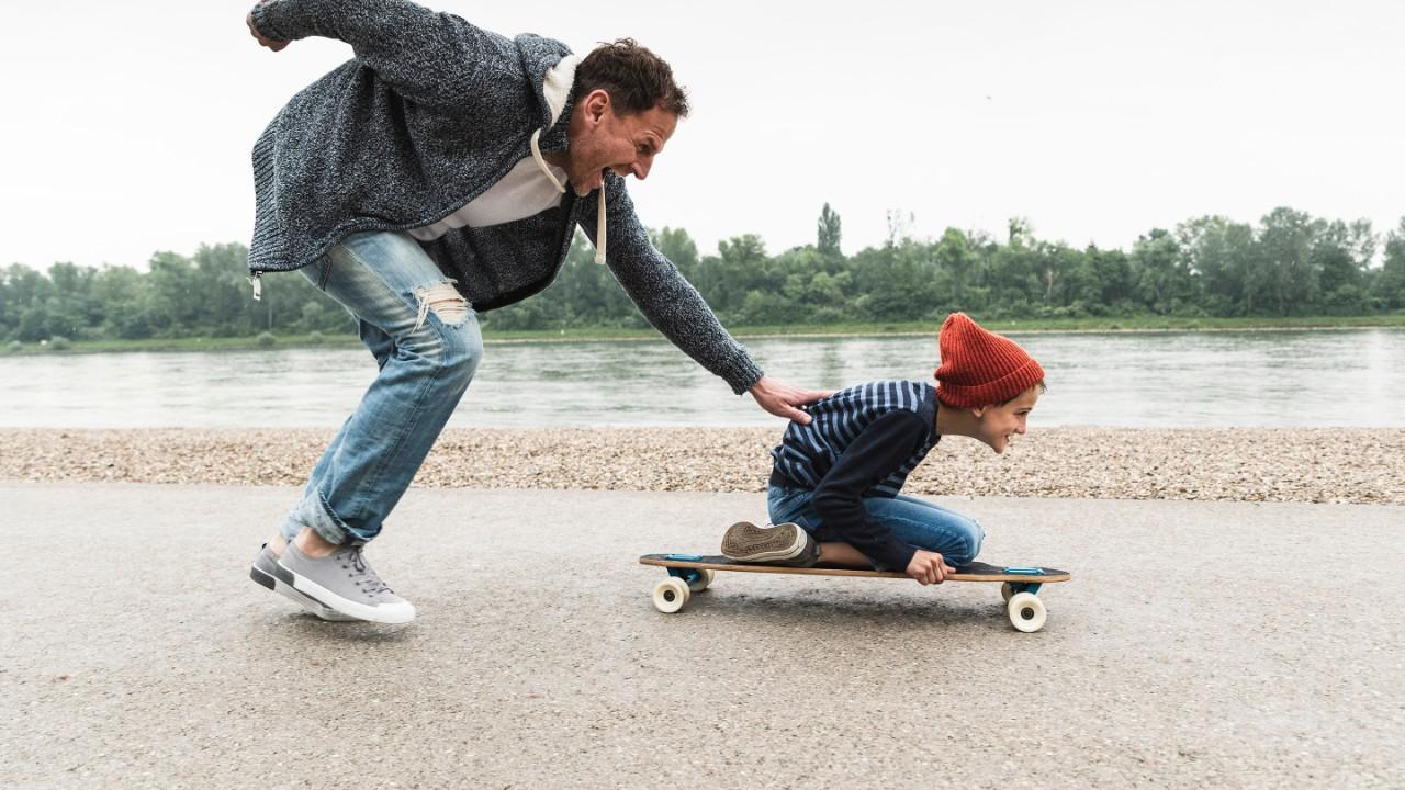 快乐的父亲推着儿子在河边玩滑板